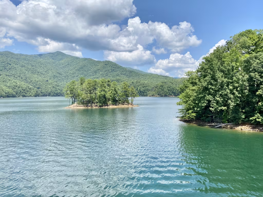 Fontana Lake in summer: green water, a small wooded island and forested mountains under white clouds