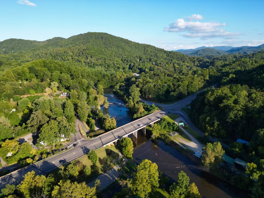 The Tuckasegee River curving through green hills under the highway bridge at Dillsboro, from the air